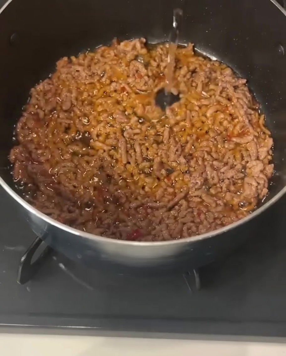 Liquido trasparente versato in una pentola contenente carne di maiale macinata cotta e condita.