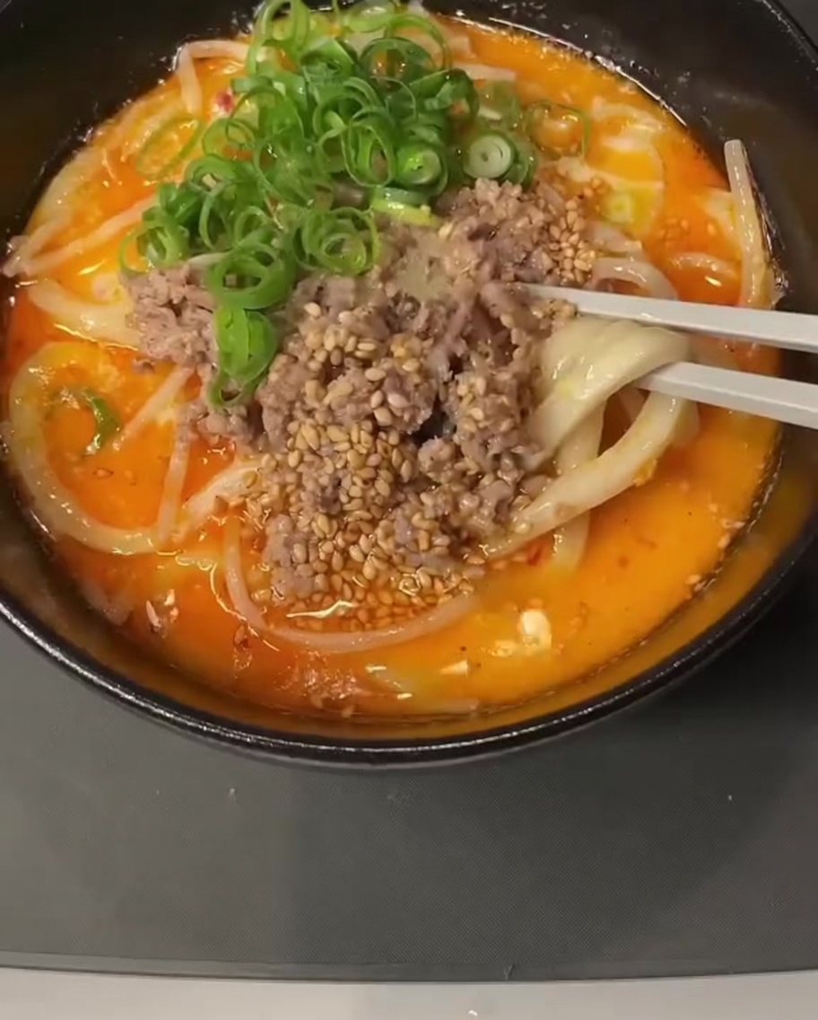 Vista ravvicinata di una pentola contenente un liquido cremoso con un cucchiaio di pasta di miso che viene mescolato.