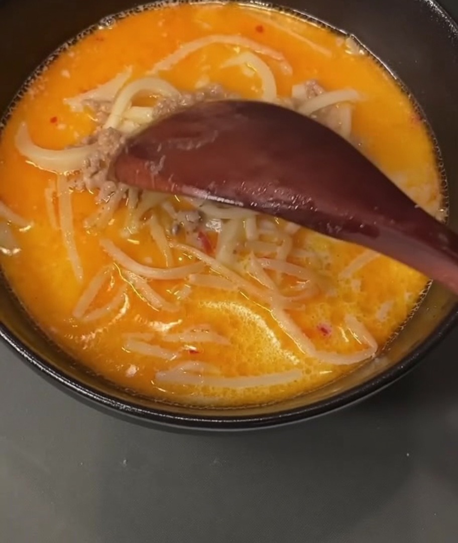 Un cucchiaio di legno raccoglie carne di maiale macinata cotta da una pentola piena di brodo.
