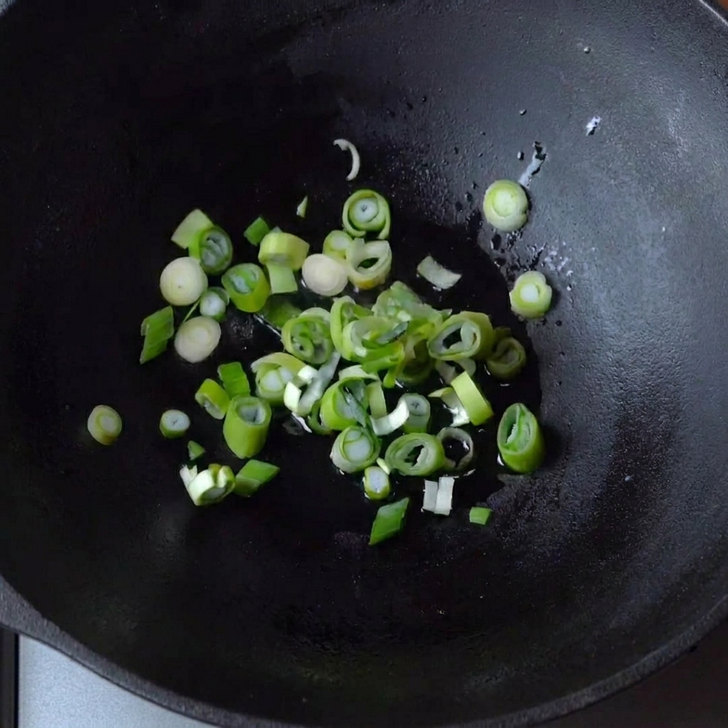 Cipollotti che sfrigolano in un po di olio in un wok di ghisa.