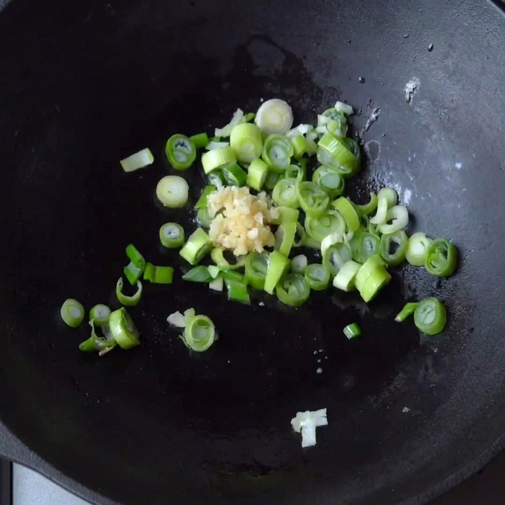 Aglio tritato aggiunto nel wok con i cipollotti in cottura.