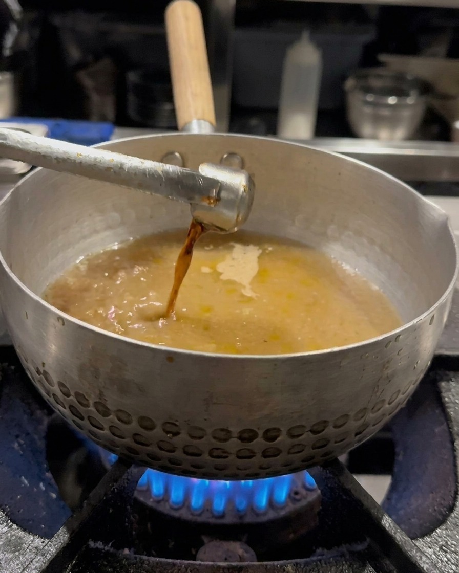 Salsa di soia versata nel brodo e mescolata con una frusta.