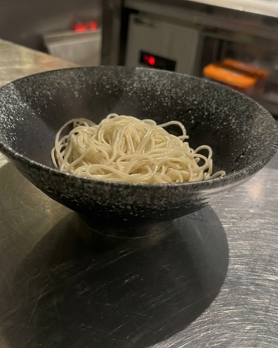 Noodle cotti in una ciotola nera su cui viene versato il brodo caldo ricco e cremoso.
