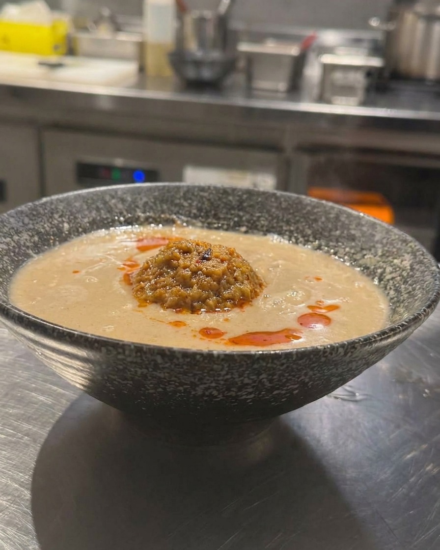 Una ciotola di Tan Tan Ramen con brodo cremoso, guarnita con carne macinata e olio al peperoncino rosso brillante.