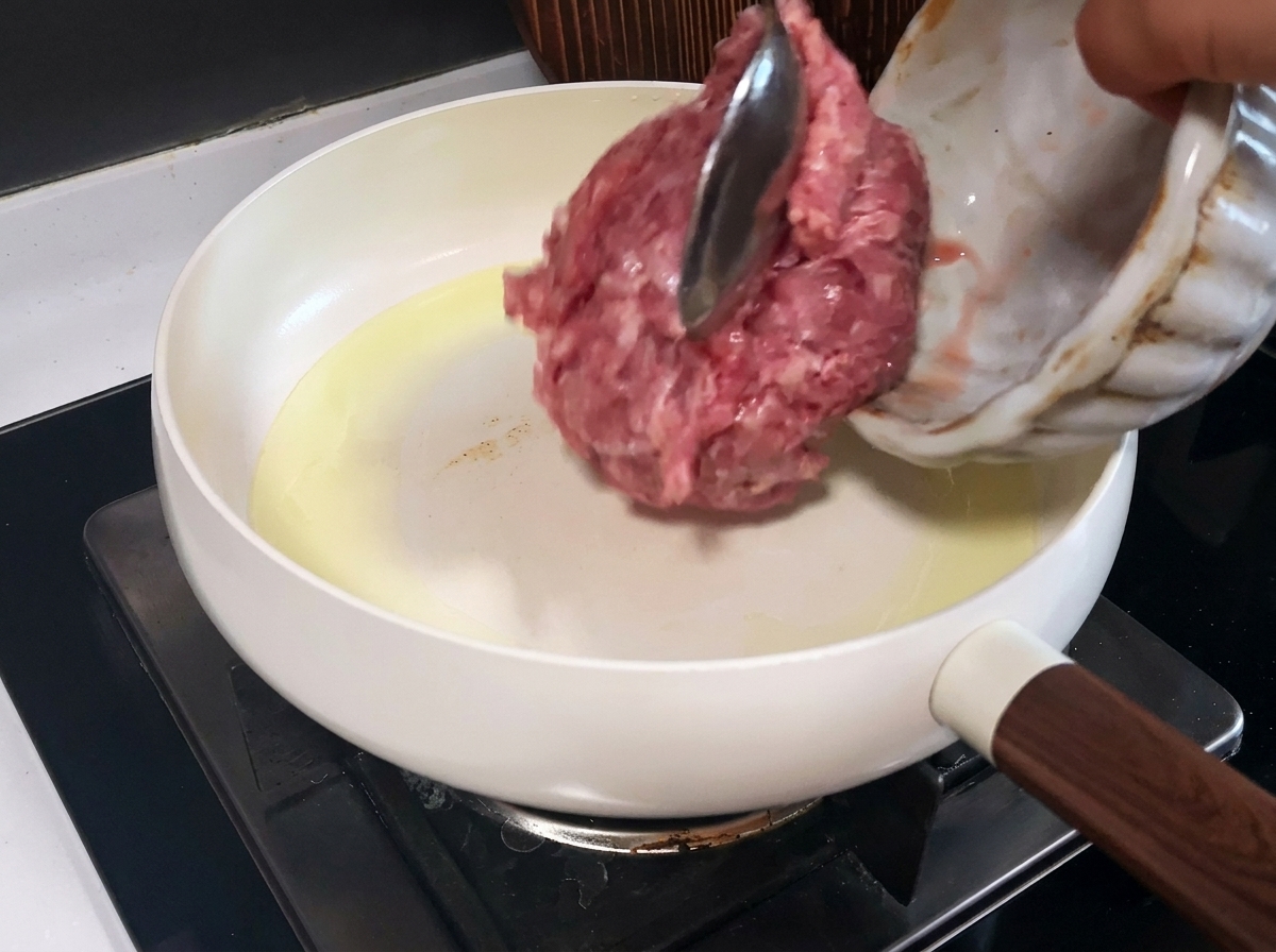 Carne di maiale macinata in cottura in una padella bianca, con pezzetti cotti e rosolati.