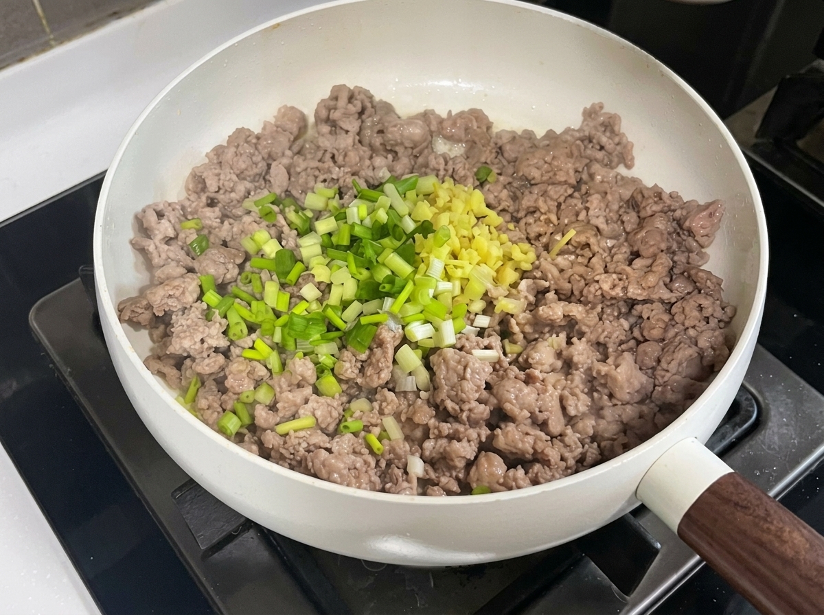 Maiale macinato in padella mescolato con aromi tritati, pasta di fagioli e pasta di soia.