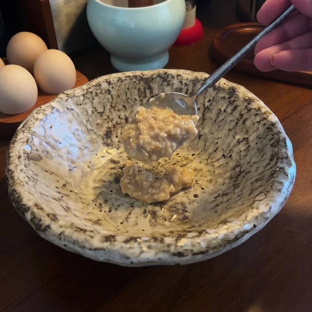 Un cucchiaio di densa pasta di miso e sesamo aggiunto a una ciotola di ceramica maculata vuota.