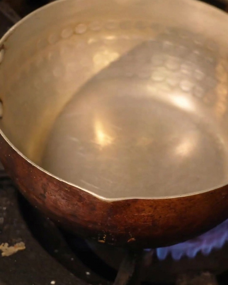 Una pentola in metallo martellato riempita di liquido che si scalda sopra il fornello.