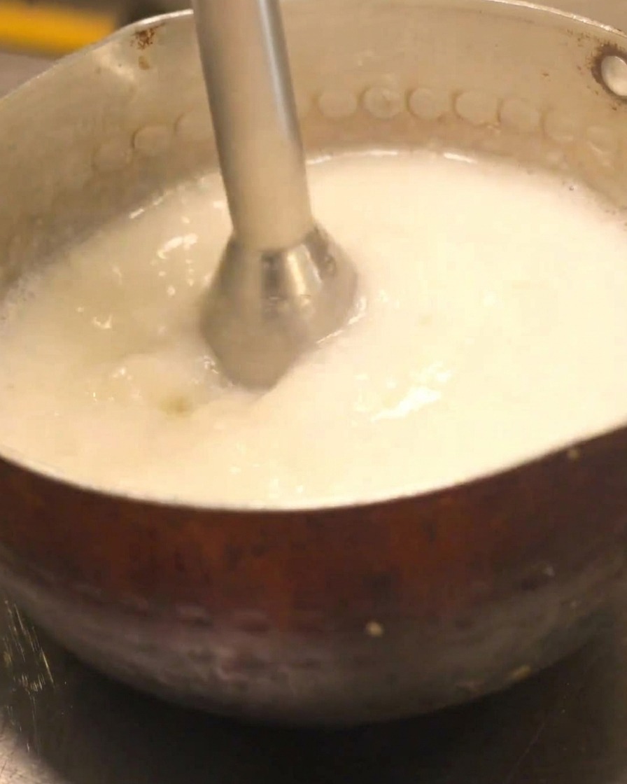 Un frullatore a mano usato per creare una schiuma cremosa in una pentola di zuppa chicken paitan.