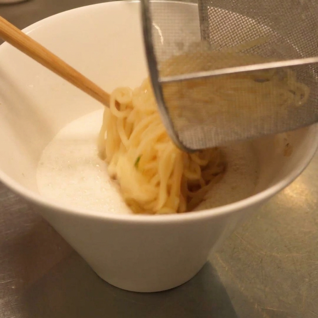 Noodle per ramen scolati trasferiti nella ciotola di zuppa cremosa usando un cestello da cucina.