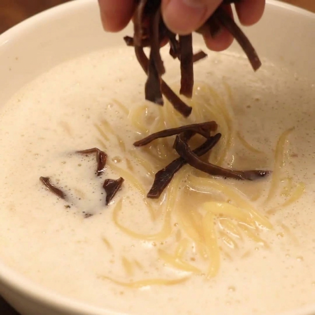 Una ciotola di Ramen Chicken Paitan Schiumoso completamente assemblata, guarnita con chashu, funghi e verdure fresche.