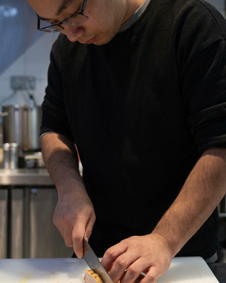 Un coltello affilato che taglia il pollo chashu cotto su un tagliere bianco.