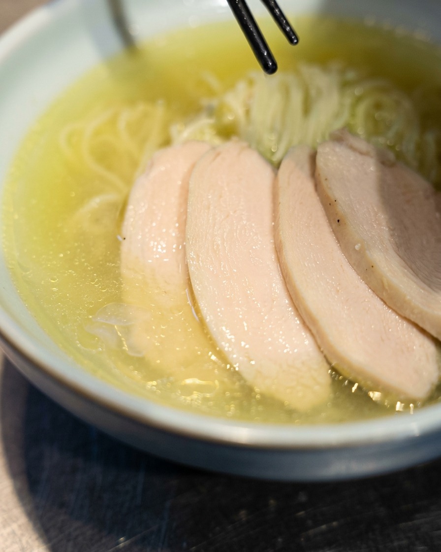 Bacchette che posizionano fette di tenero pollo chashu sopra i ramen appena preparati in una ciotola.