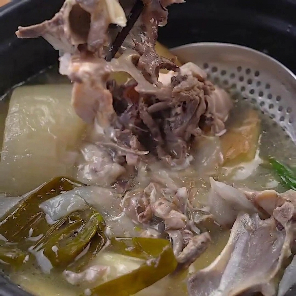 Carne di pollo tenera staccata dalle ossa cotte nella pentola a pressione usando bacchette nere.