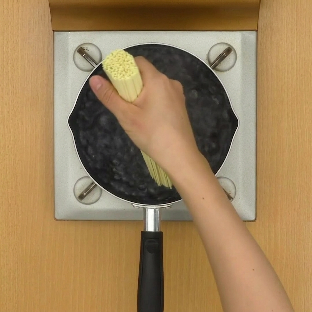 Noodles per ramen in ebollizione in una pentola dacqua, mescolati con le bacchette.