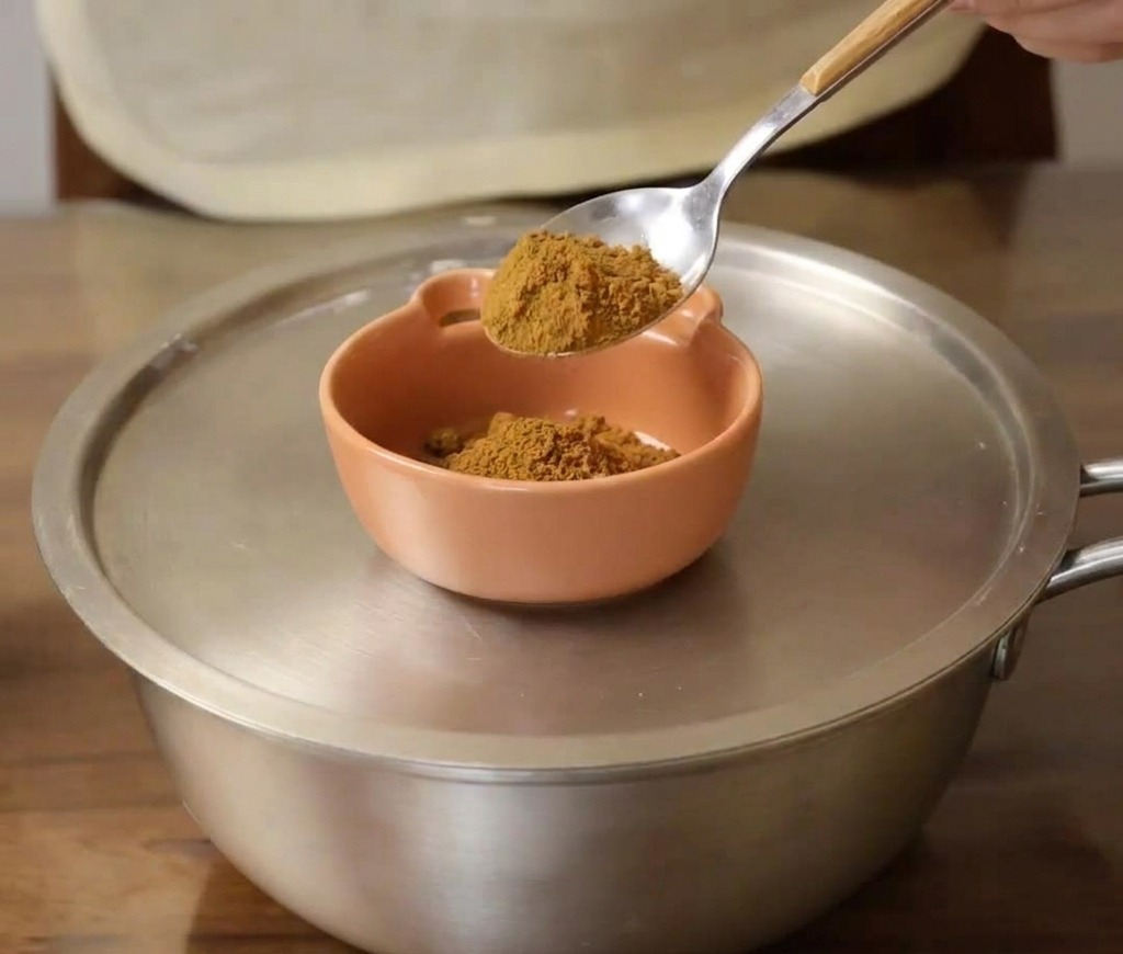 Un cucchiaio di polvere di senape aggiunto a una piccola ciotola di ceramica arancione.