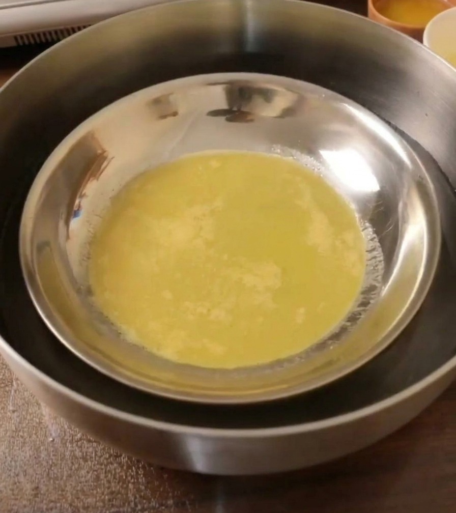 Un foglio di pasta cotta ed elastica allinterno di un piatto di metallo in raffreddamento in un bagno dacqua.