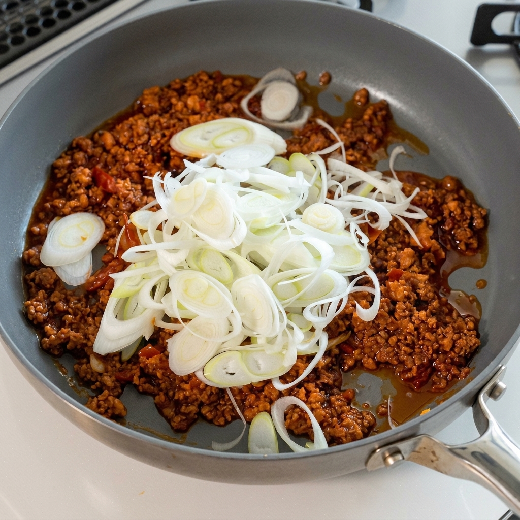 Una grande manciata di cipollotto affettato aggiunto al ragù di carne.