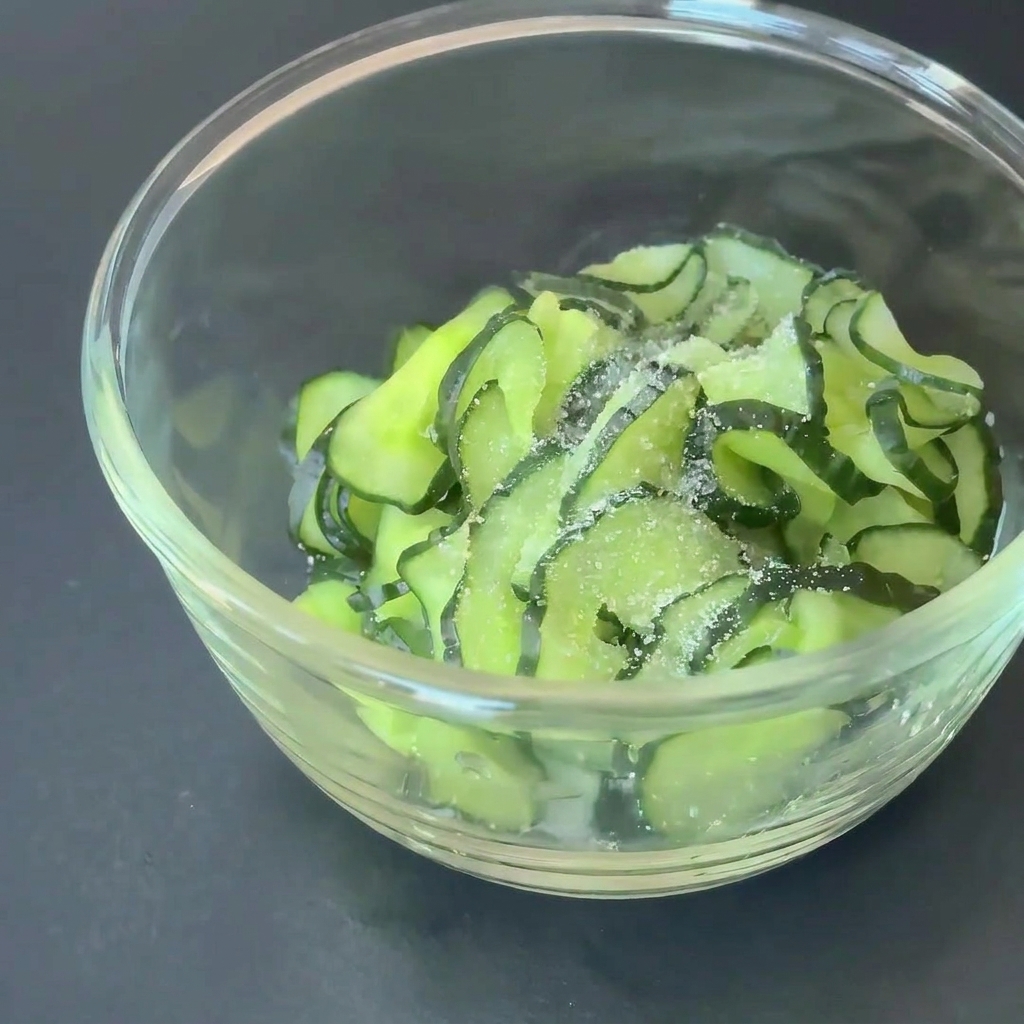 Fette di cetriolo in una ciotola di vetro condite con zucchero e aceto di mele.