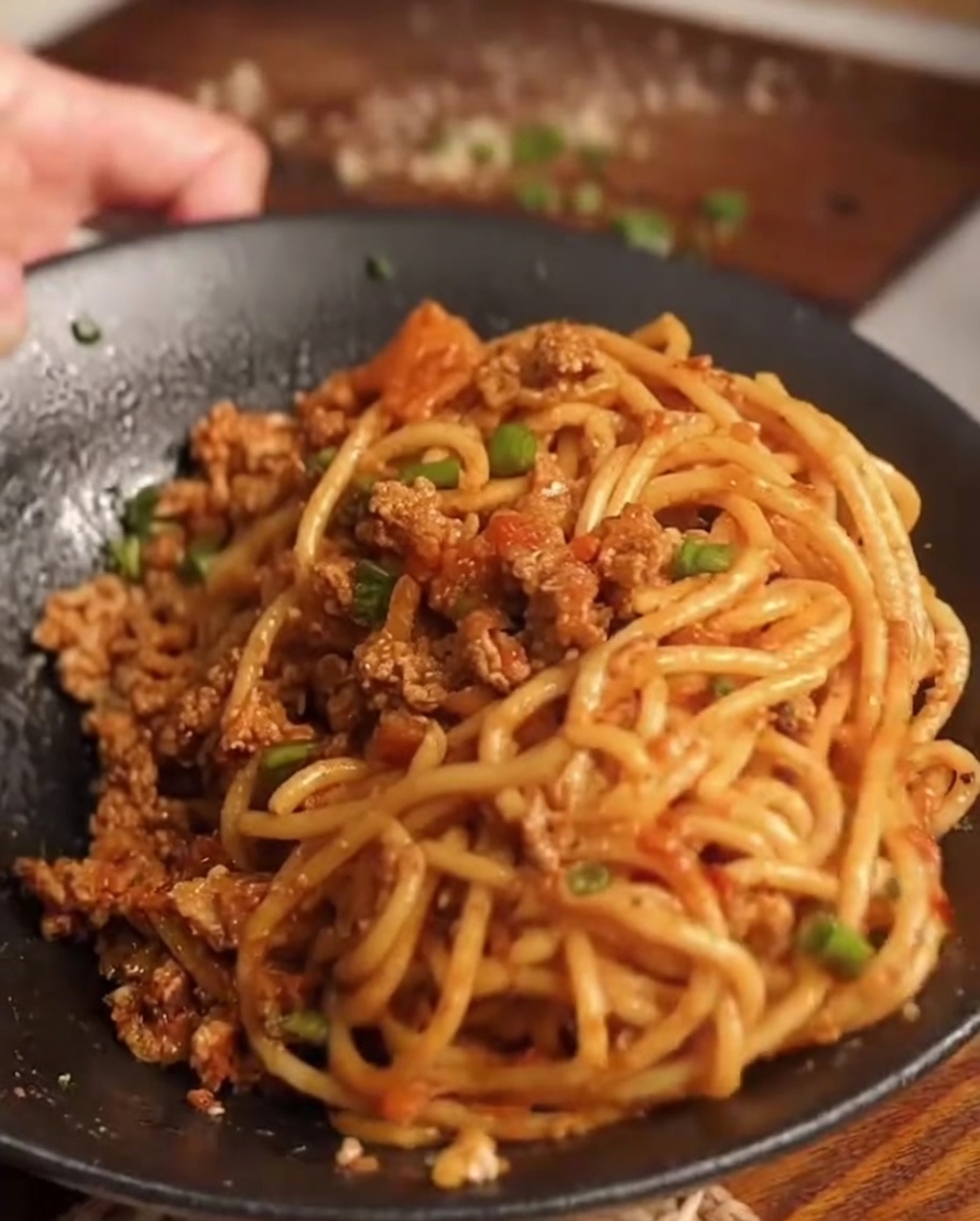 Spaghetti appena cotti posti nella padella contenente il sugo preparato di carne e carote.