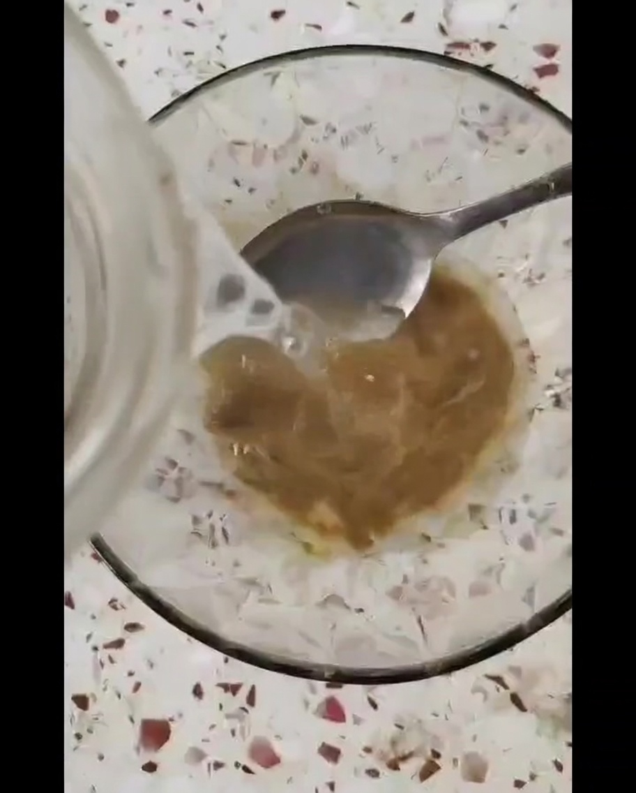 Una piccola ciotola in vetro contenente una salsa densa color marrone, mescolata con un cucchiaio di metallo.