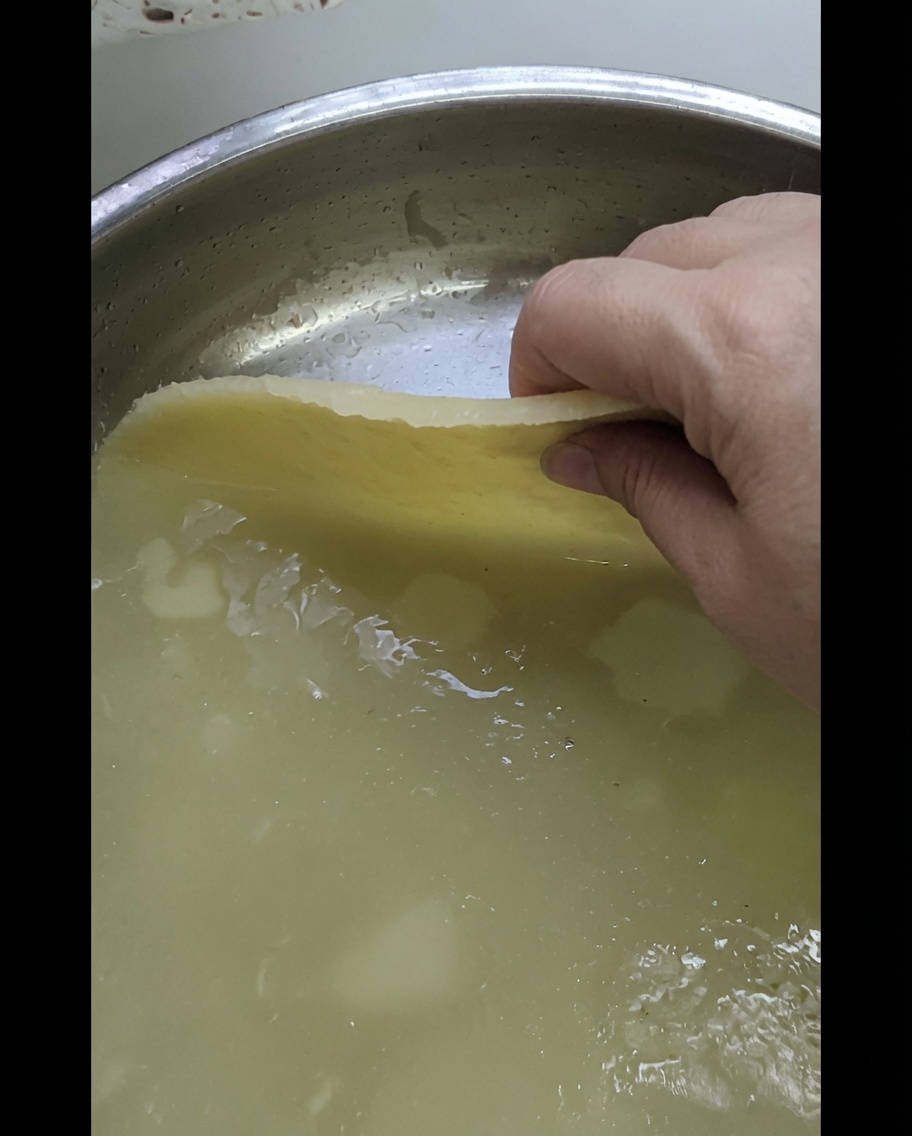 Una mano che posiziona un foglio di impasto steso su una teglia in metallo lucido.