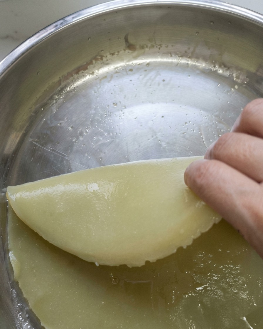 Un pezzo di impasto cotto al vapore tagliato a strisce lunghe e uniformi su un tagliere.