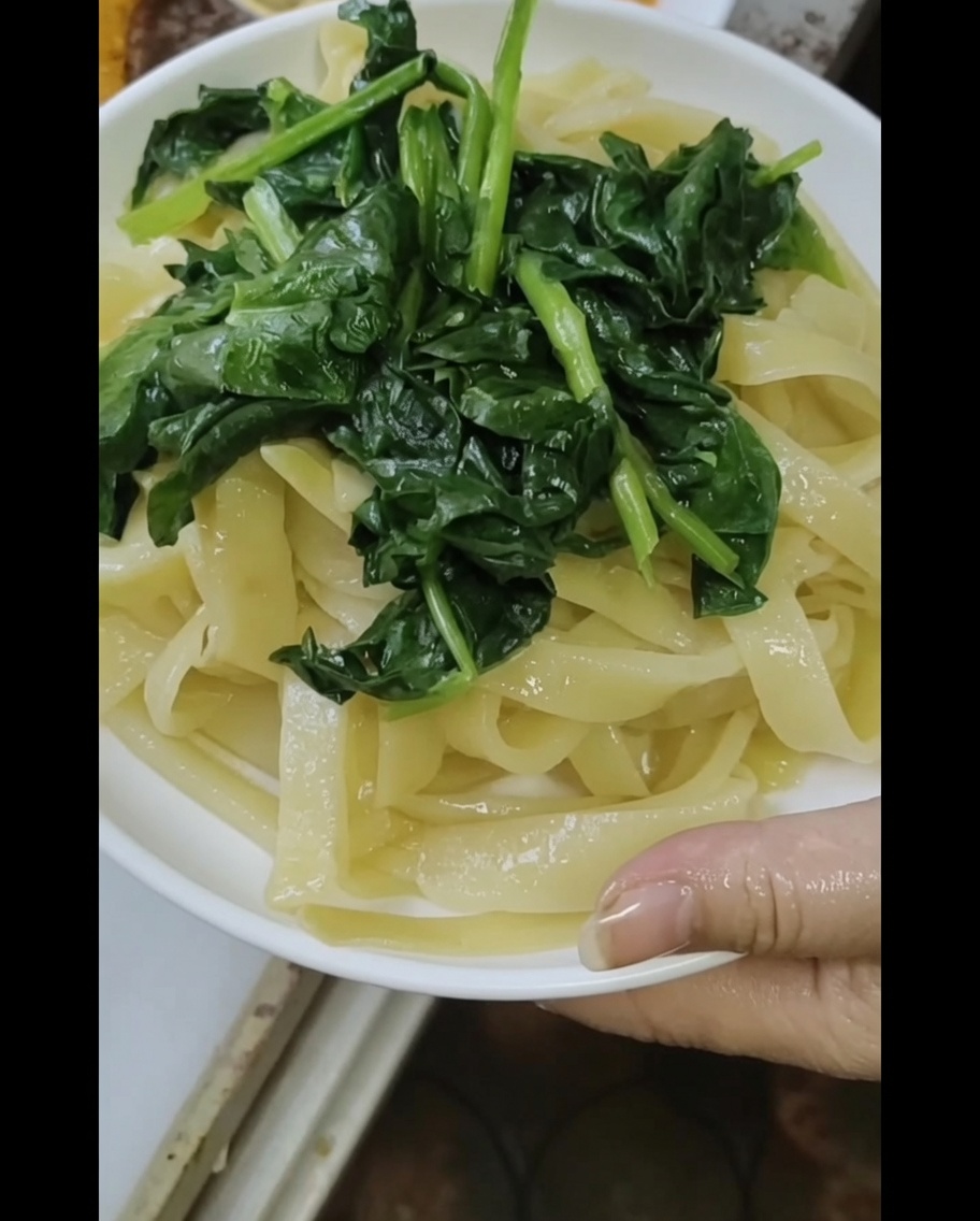 Vista ravvicinata di noodles al vapore con spinaci, mentre viene versata la ricca salsa al sesamo e arachidi.