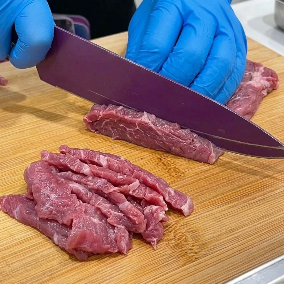 Primo piano di girello di manzo tagliato a fettine sottili su un tagliere di legno.