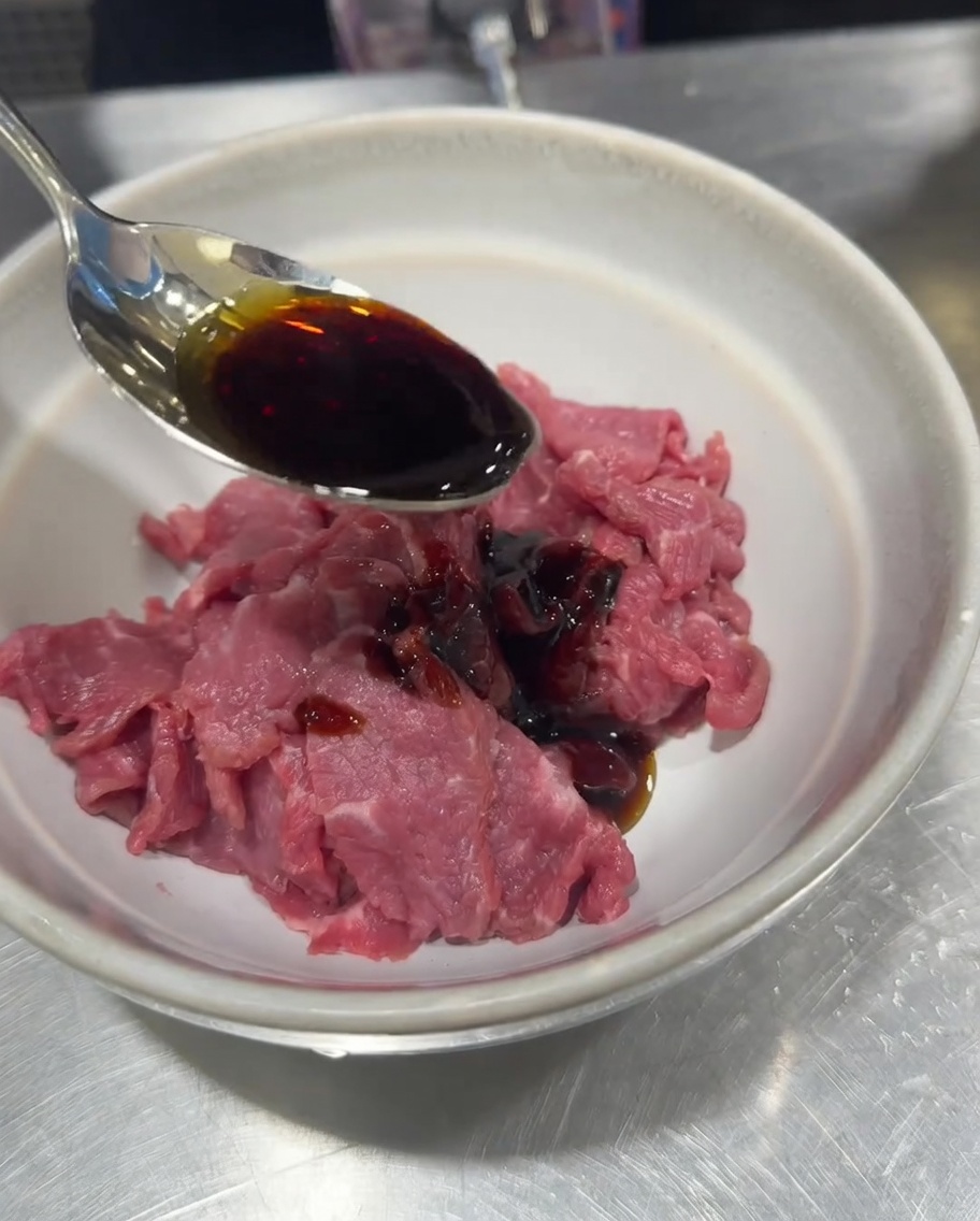 Manzo crudo a fette in una ciotola condito con salsa di soia, sale, pepe e fecola di mais.