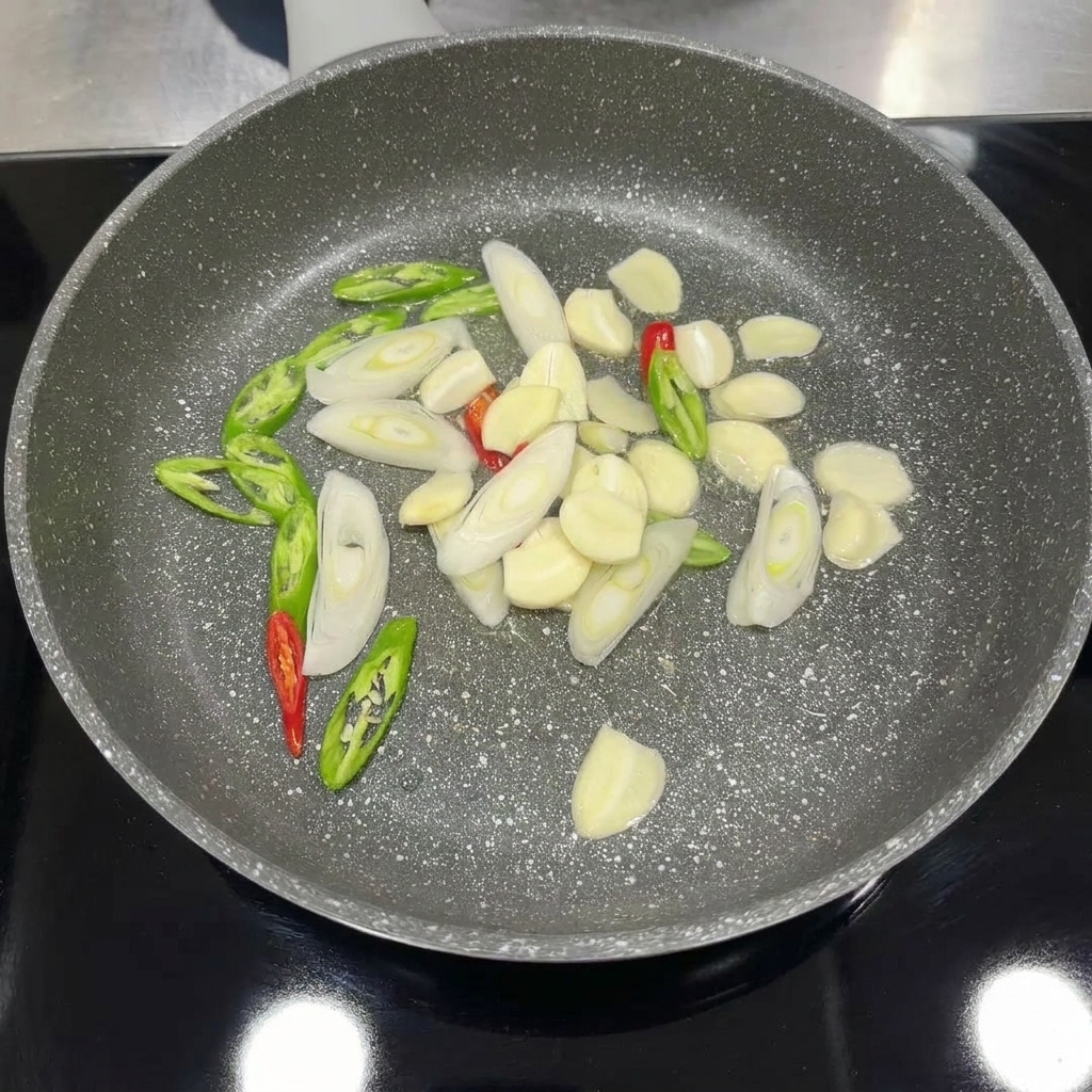 Aglio, peperoncino e cipollotti affettati che soffriggono in padella fino a diventare profumati.