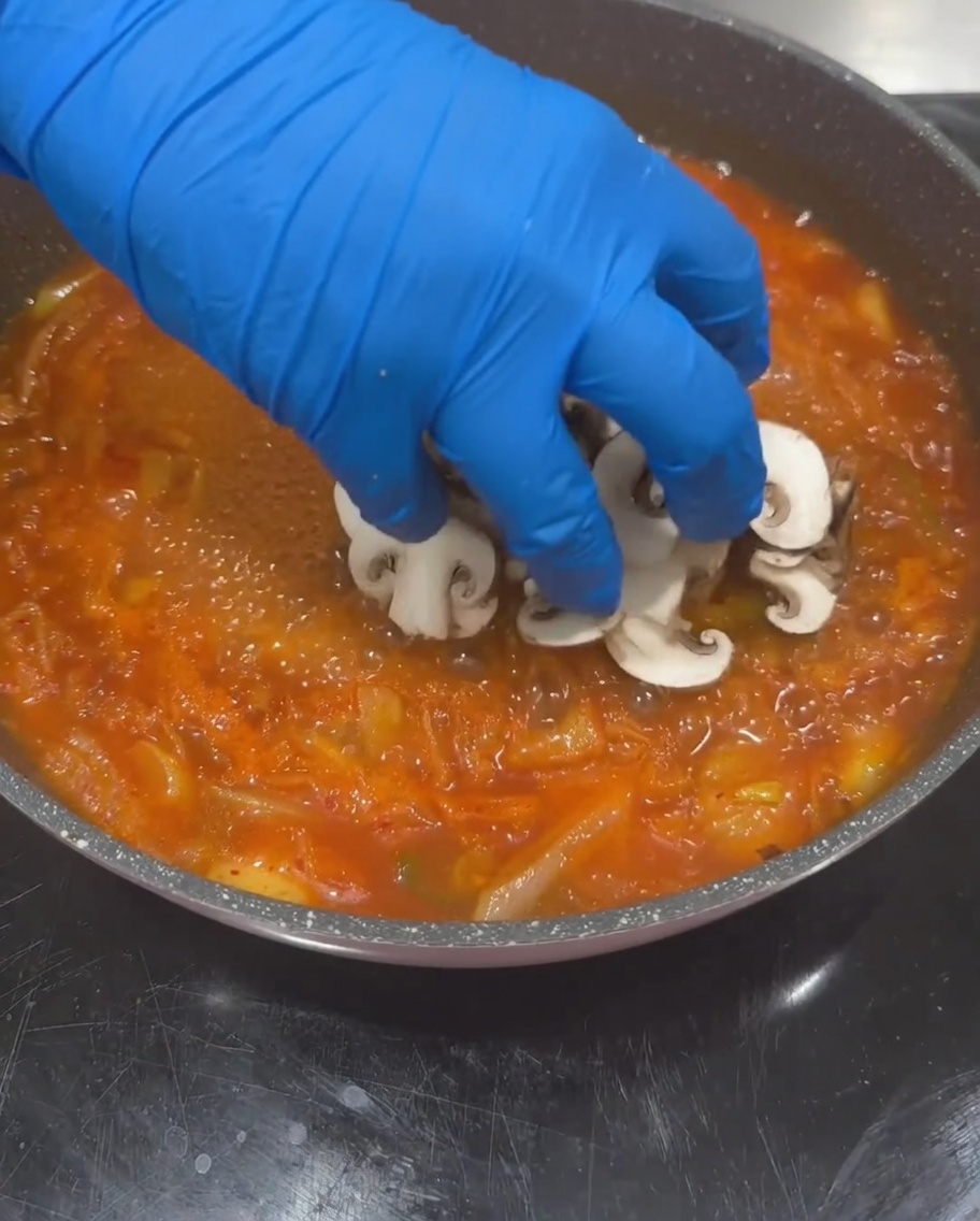 Funghi shiitake a fette, zucchine e cubetti di tofu aggiunti alla base di zuppa di kimchi in ebollizione.