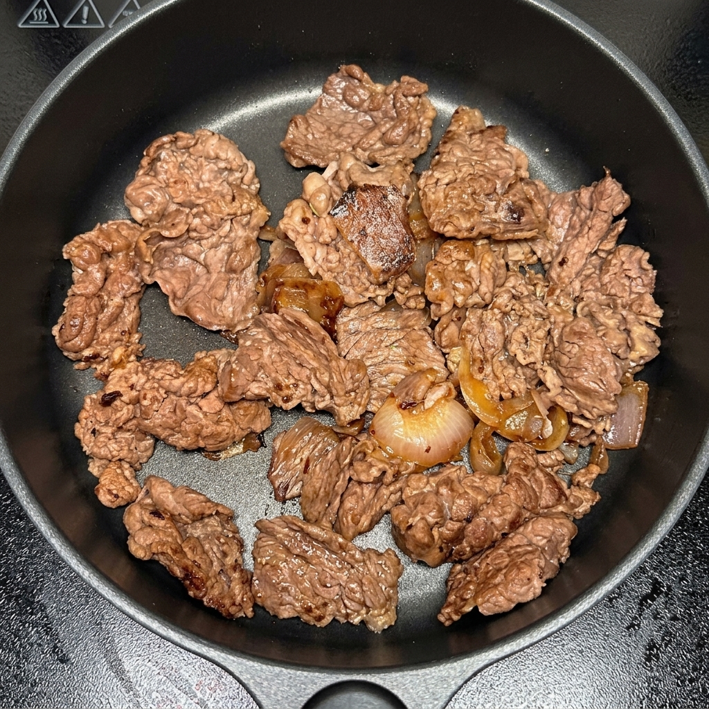 Pezzi di kimchi aggiunti alla padella con manzo e cipolle.