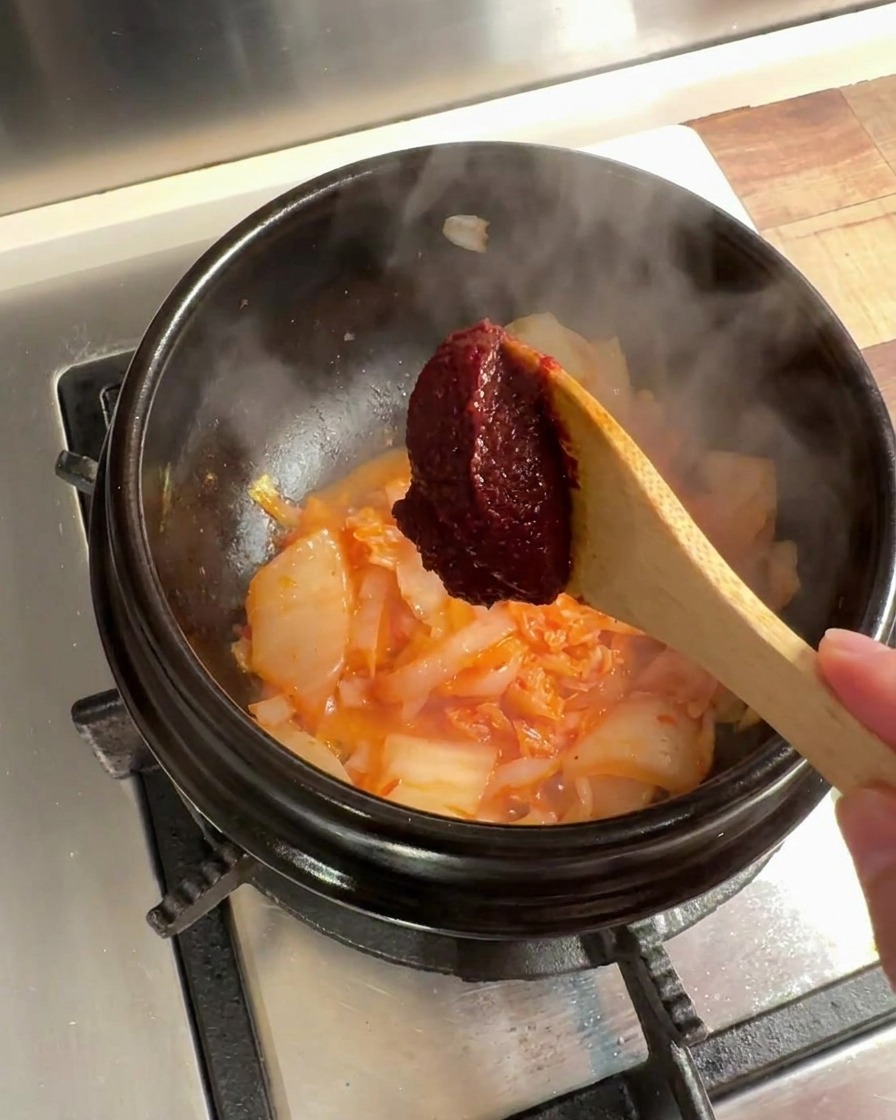 Un cucchiaio di pasta di peperoncino coreana aggiunta al composto di kimchi e cipolle.