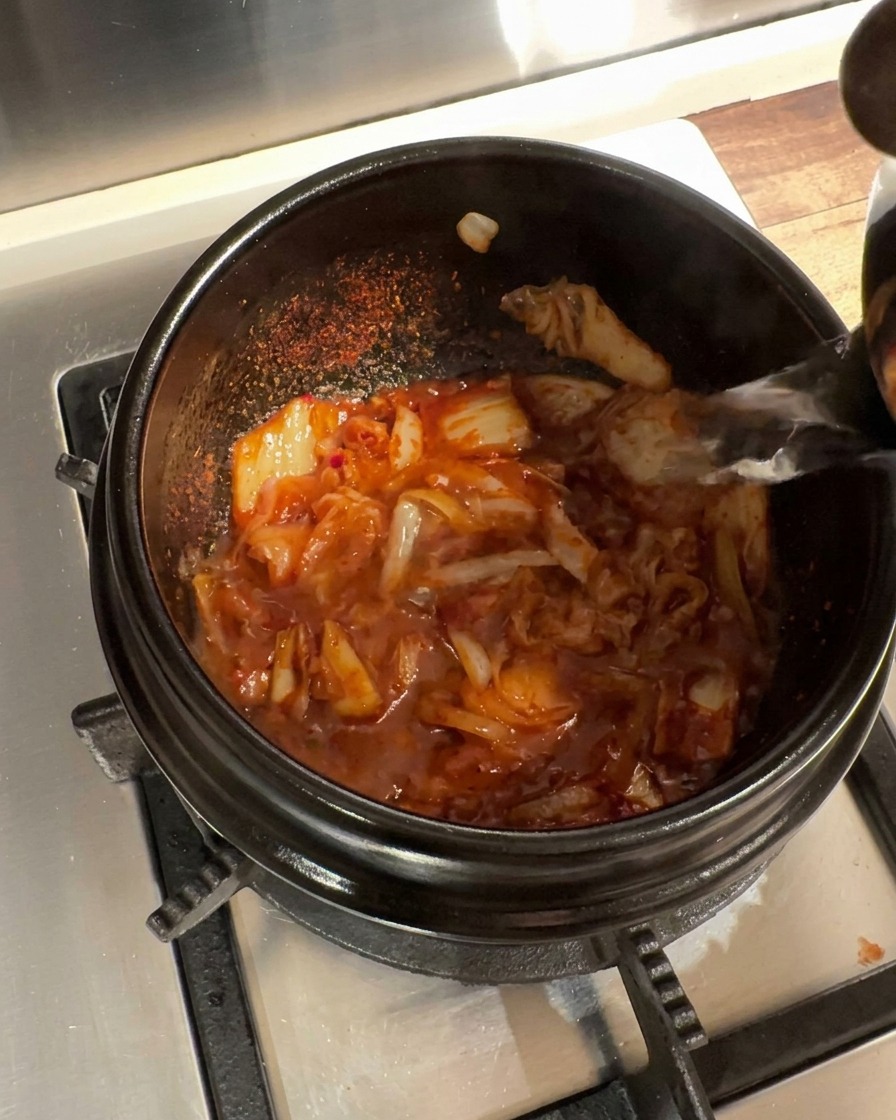 Acqua calda versata nella pentola di pietra con la base di kimchi e cipolla.