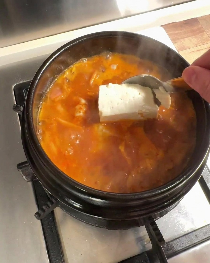 Grandi pezzi di tofu fresco aggiunti nel brodo di kimchi in ebollizione.