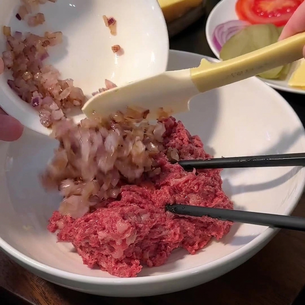 Una ciotola contenente macinato di manzo, pangrattato, sale, pepe e cipolle saltate prima di mescolare.