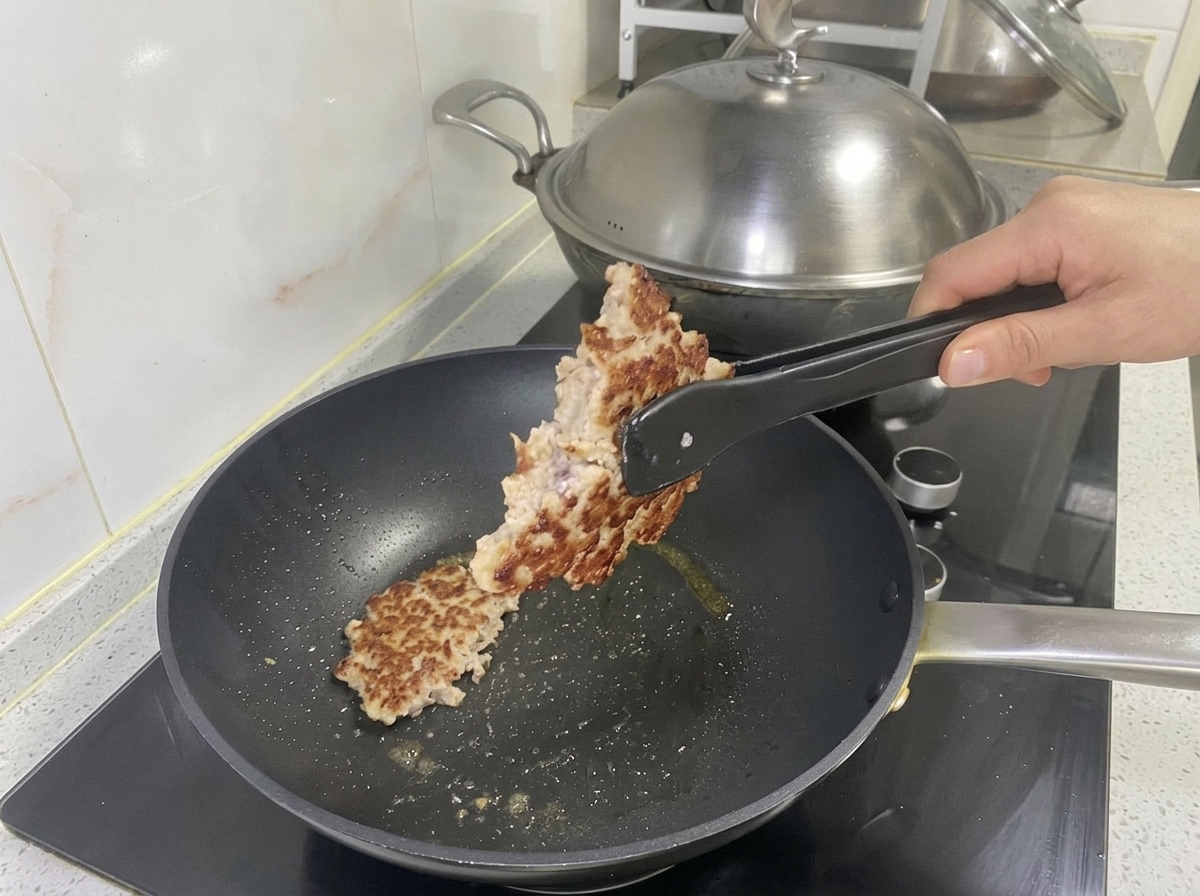Hamburger di maiale dorato sollevato dalla padella con le pinze.