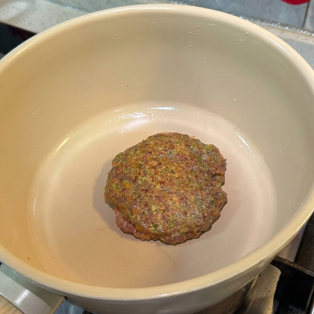 Un hamburger condito che cuoce in padella, mostrando una superficie ben rosolata.
