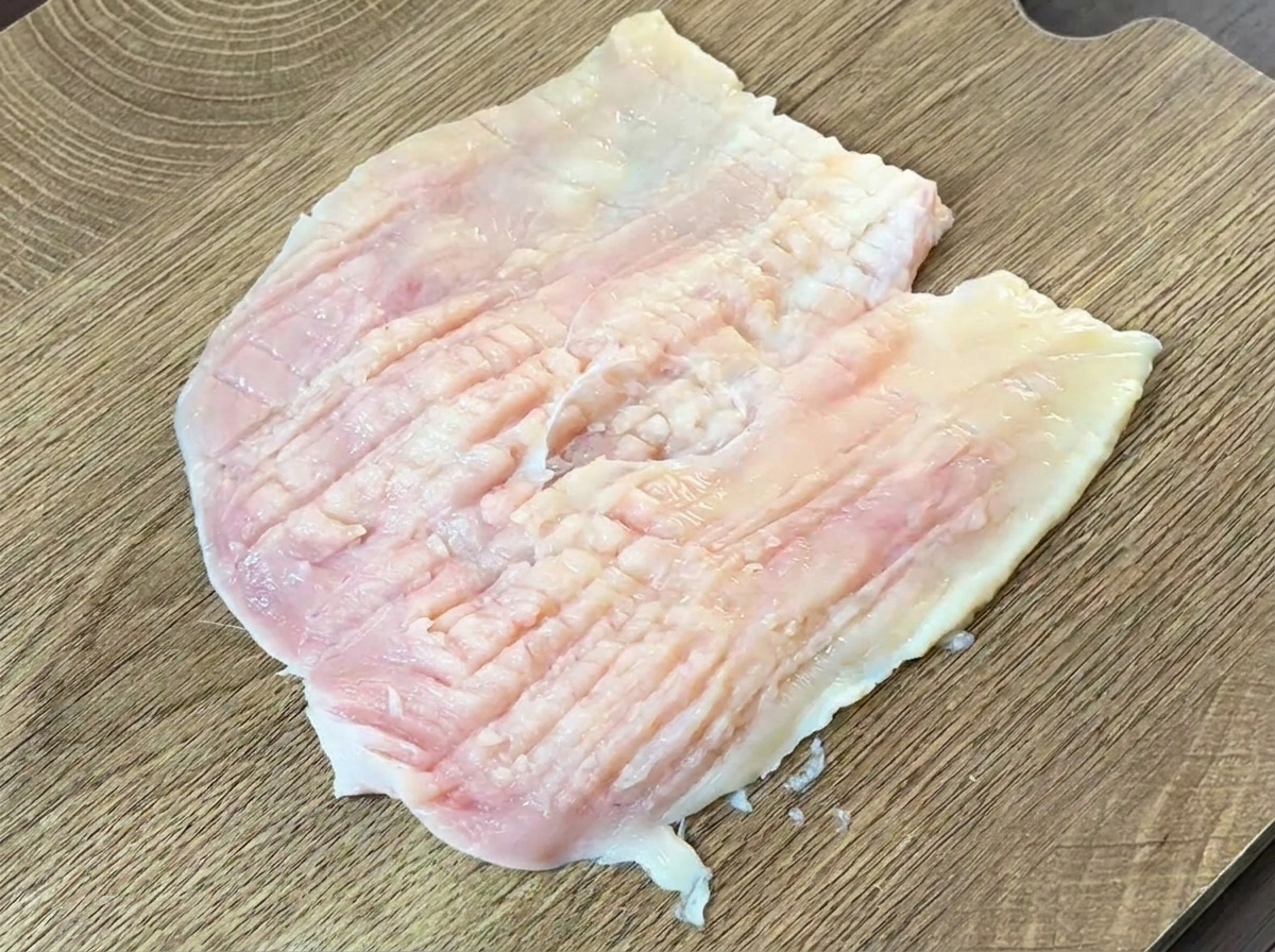 Il dorso di un coltello pesante utilizzato per battere e appiattire un petto di pollo crudo aperto a libro.