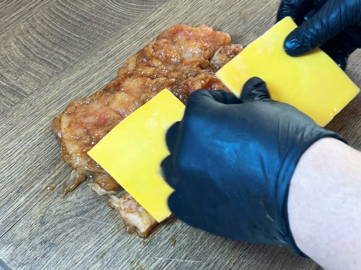 Fette di formaggio giallo posizionate al centro del petto di pollo crudo e marinato.