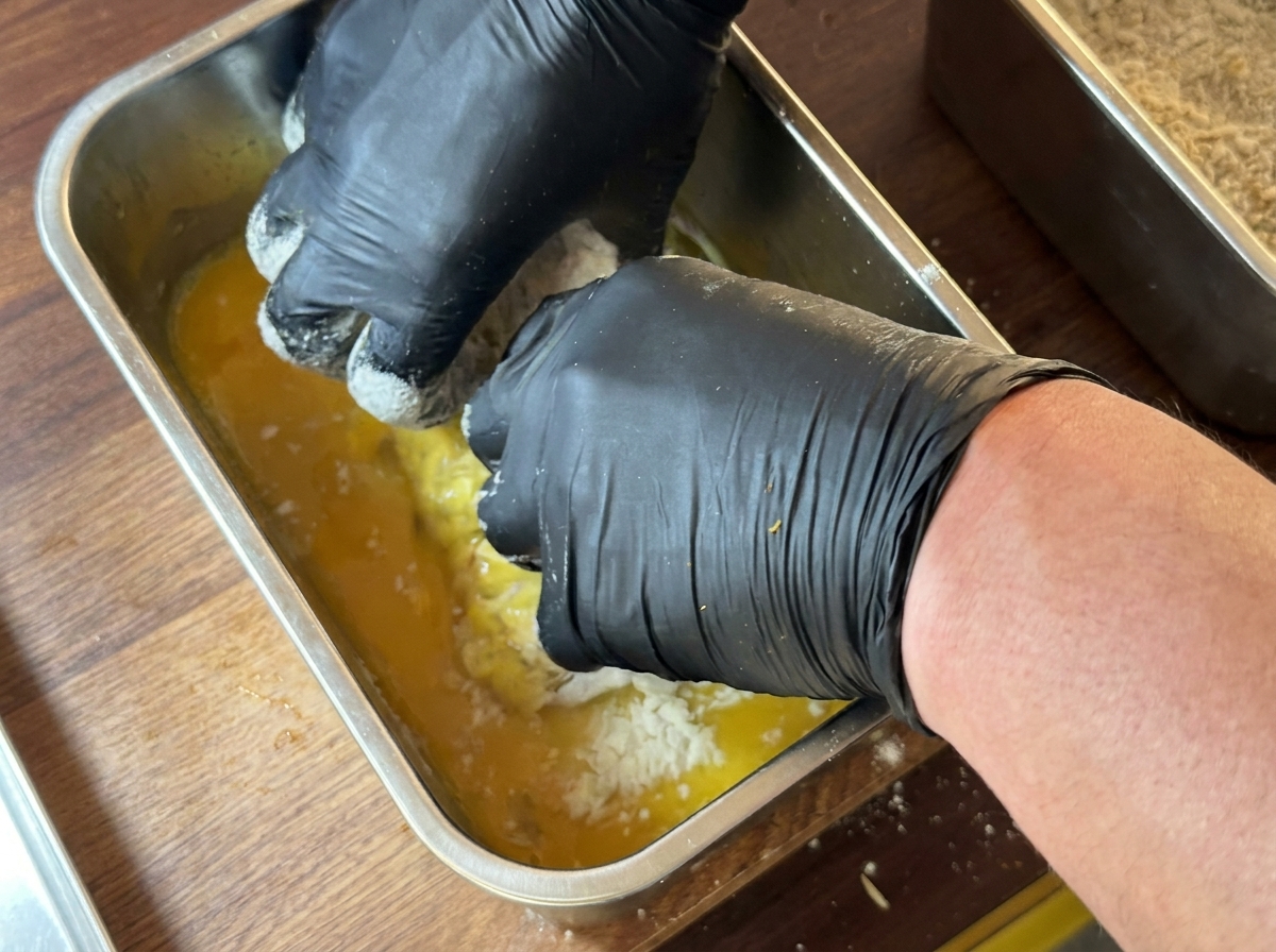 Un pezzo di petto di pollo completamente immerso in un contenitore di uovo sbattuto.