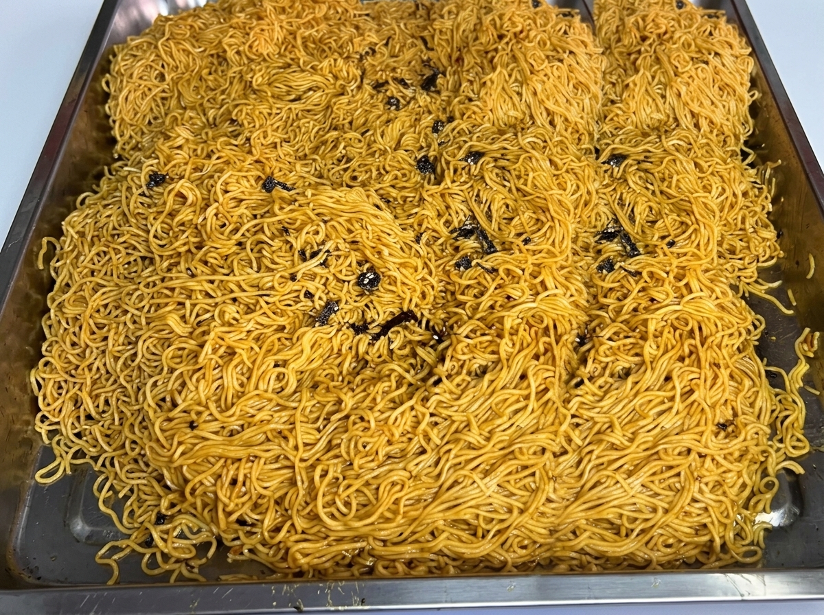 Una grande porzione di noodles cotti disposti in un vassoio di acciaio.