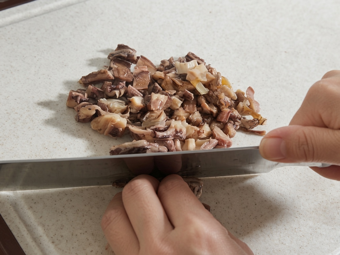 Mani che usano un grande coltello per tagliare shiitake reidratati e pezzi di polpo su un tagliere bianco.