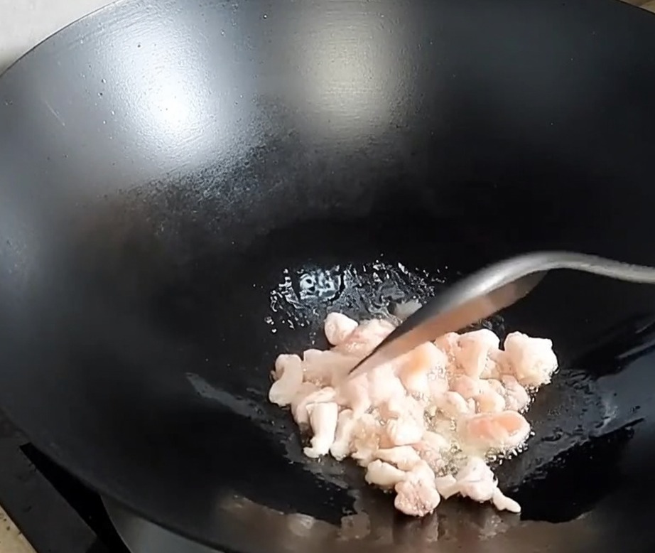 Pancetta di maiale a cubetti che rosola e rilascia il grasso in un wok caldo.