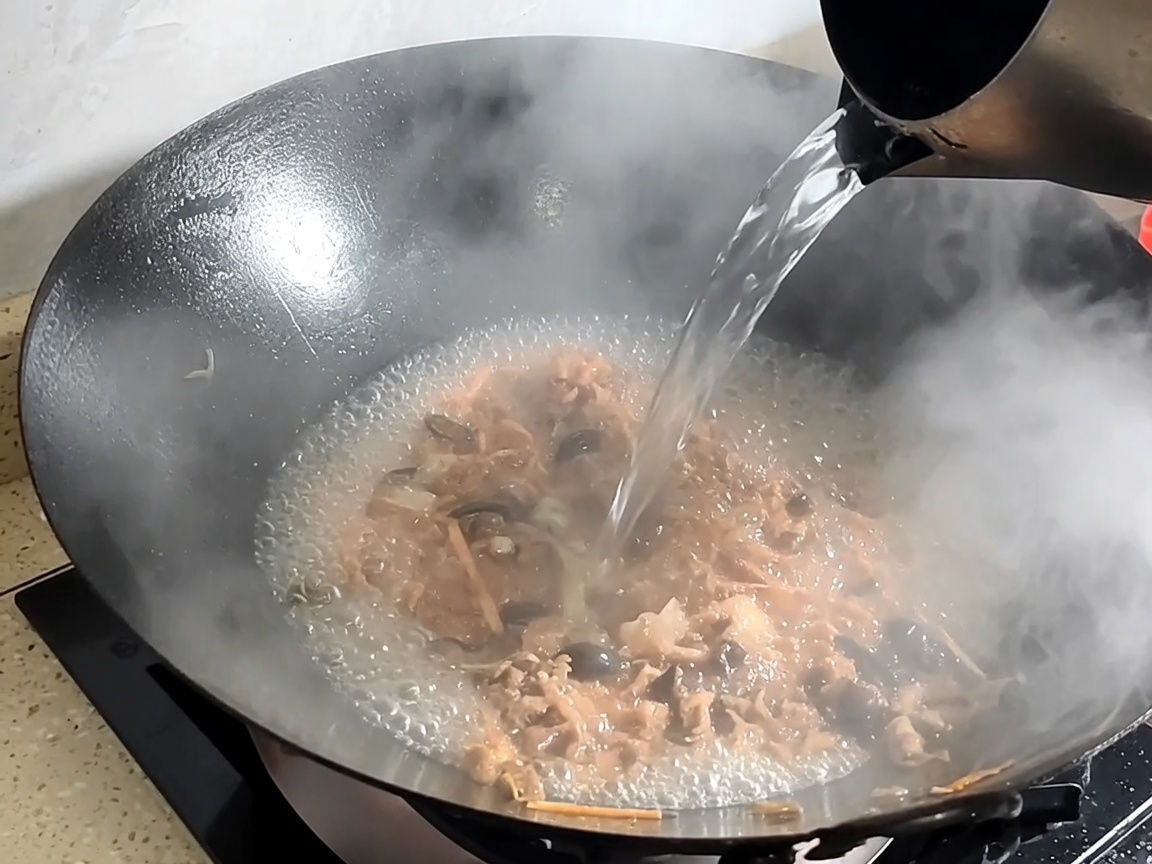 Acqua versata nel wok con maiale e funghi saltati per formare il brodo.