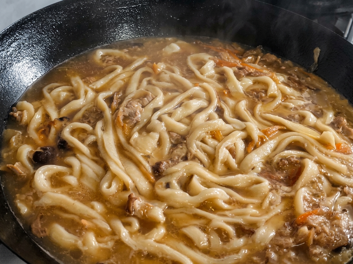 Foglie di perilla tritate sparse sopra i noodles e la zuppa che sobbolle nel wok.