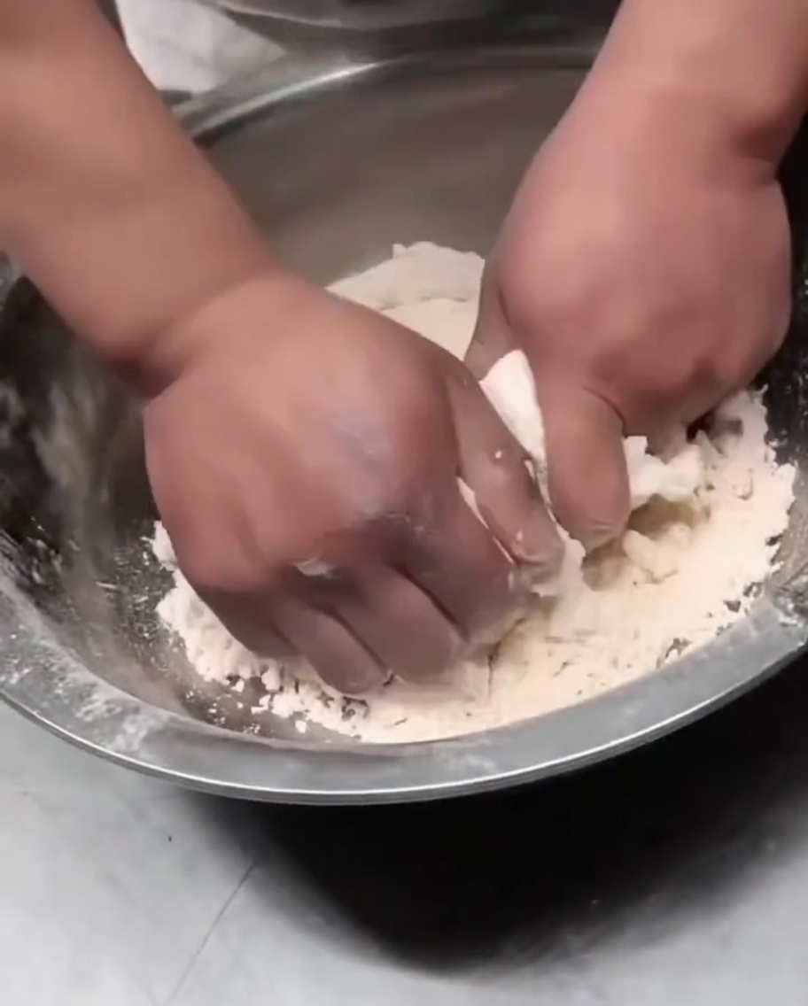 Mani che premono i fiocchi di impasto insieme per formare una palla coesa.