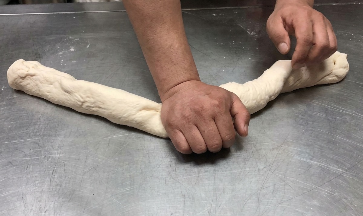 Impasto allungato e lavorato in una lunga corda su una superficie di lavoro in acciaio inox.