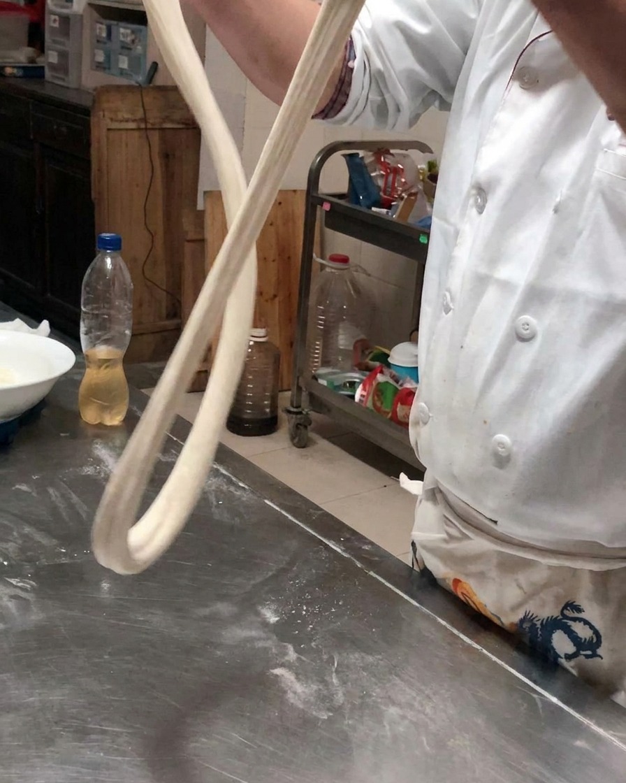 Una lunga corda di impasto tenuta in aria per lasciarla allungare sotto il proprio peso.